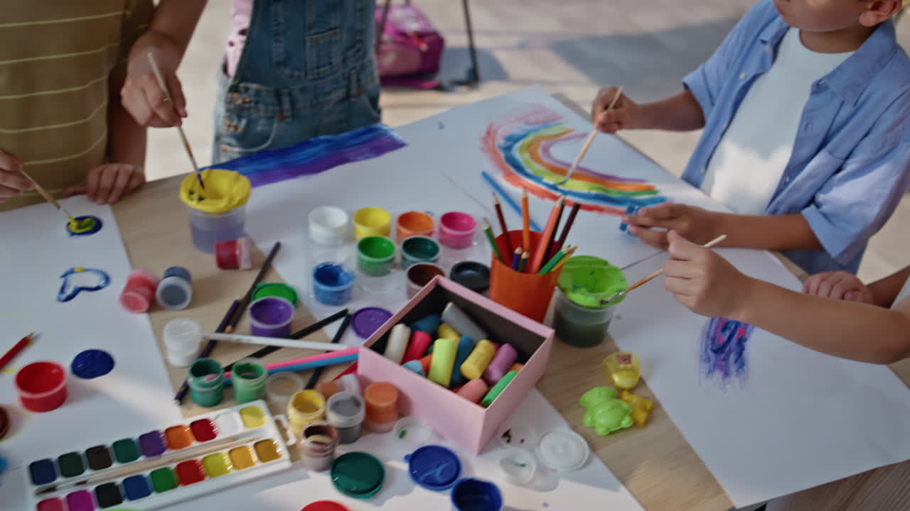 Creative school children painting at art lesson on classroom desk. Group pupils