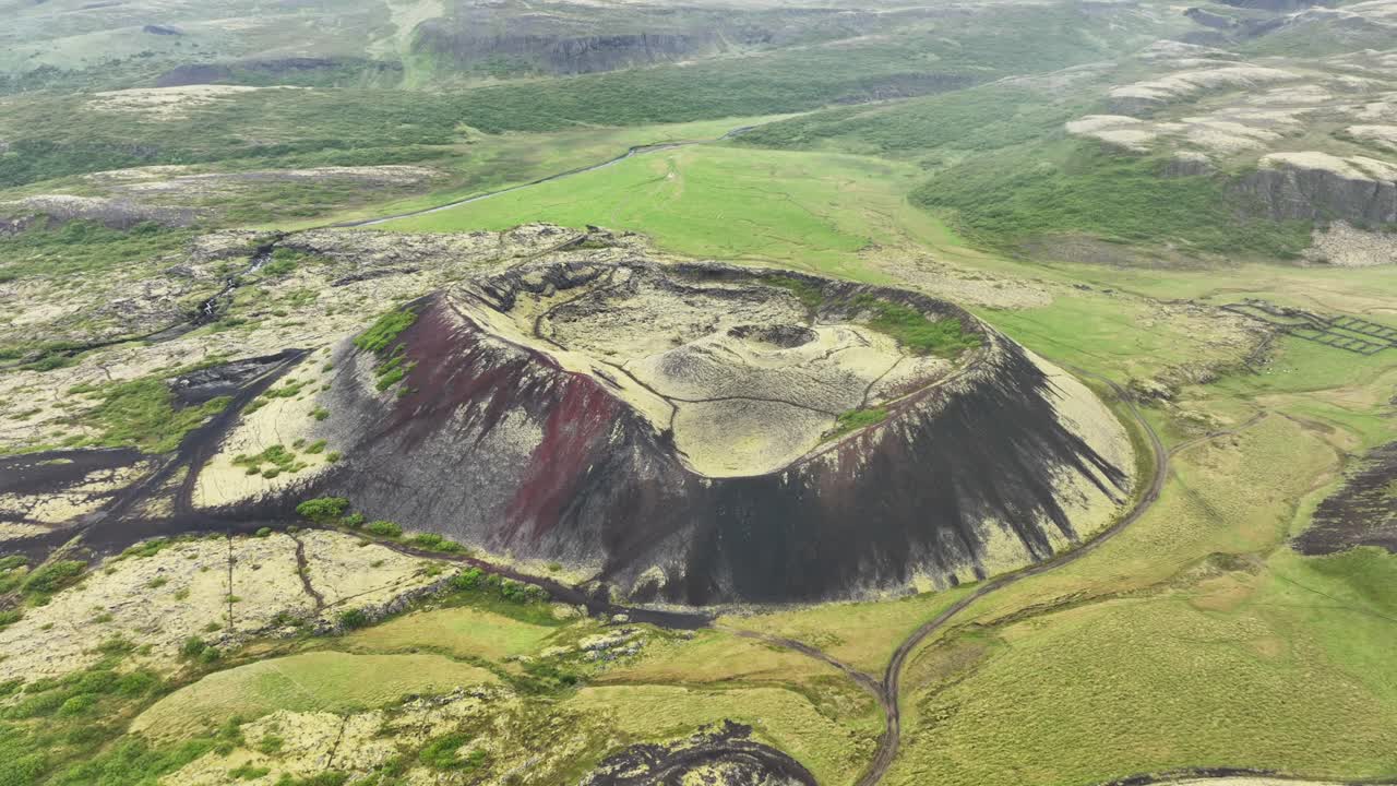 Aerial approaching Shot of Grabrok volcano crater on Iceland island. Green volcanic landscape with plants and moss in summer. Wide shot. Pathways for hiking
