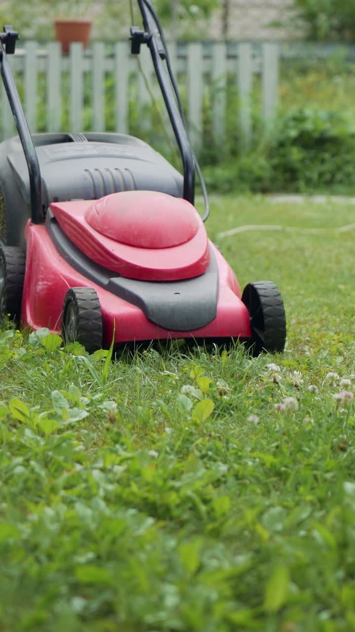 Boy running with a lawn mower in the garden. Mowing grass in the garden. Close-up Vertical video