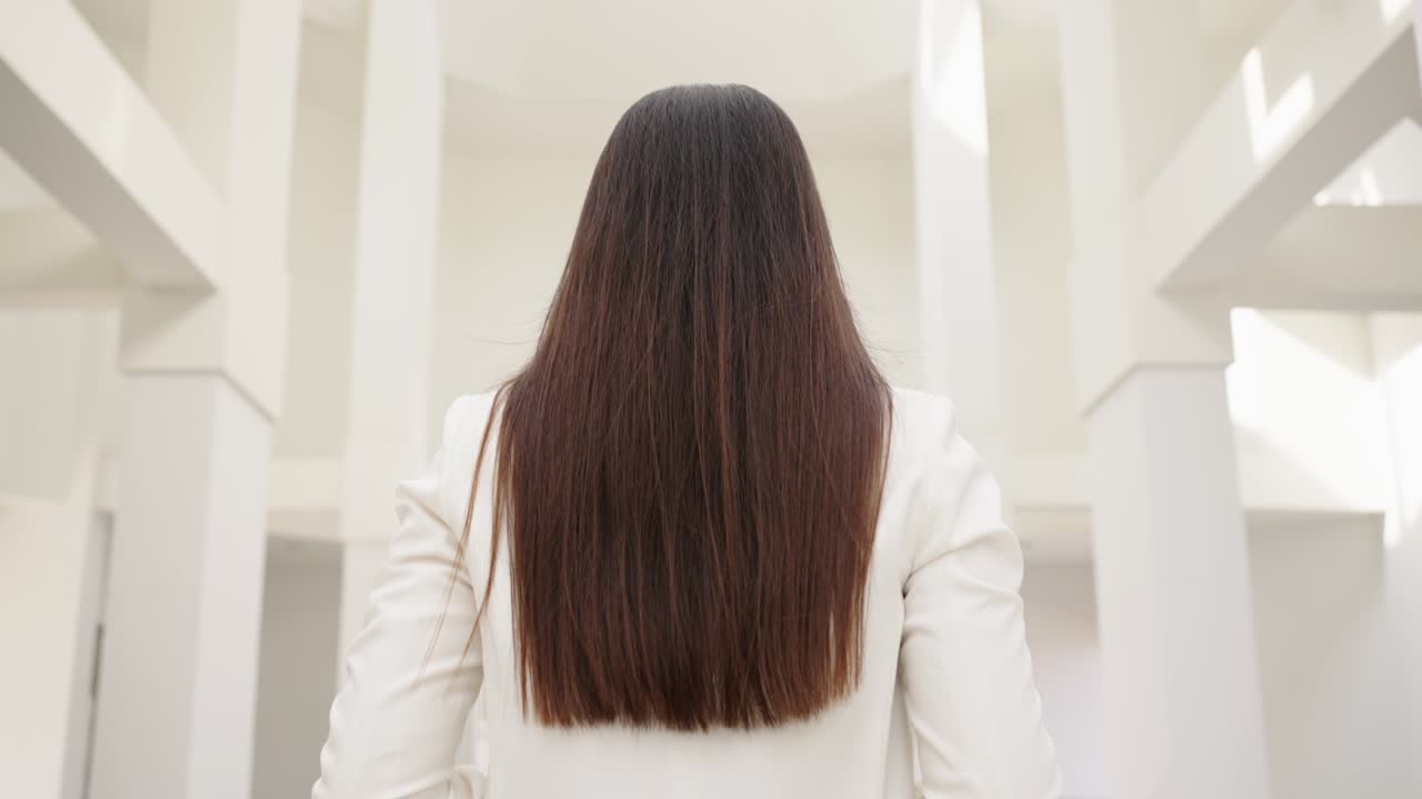 중년의 아름다운 아시아 사업가 여성이 사업 건물 사이를 걸어가며 기으로 미소 짓고 있습니다.