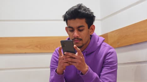 Man-using-his-smartphone-closely-to-his-face-using-two-hands-in-a-purple-hoodie,-handheld-closeup