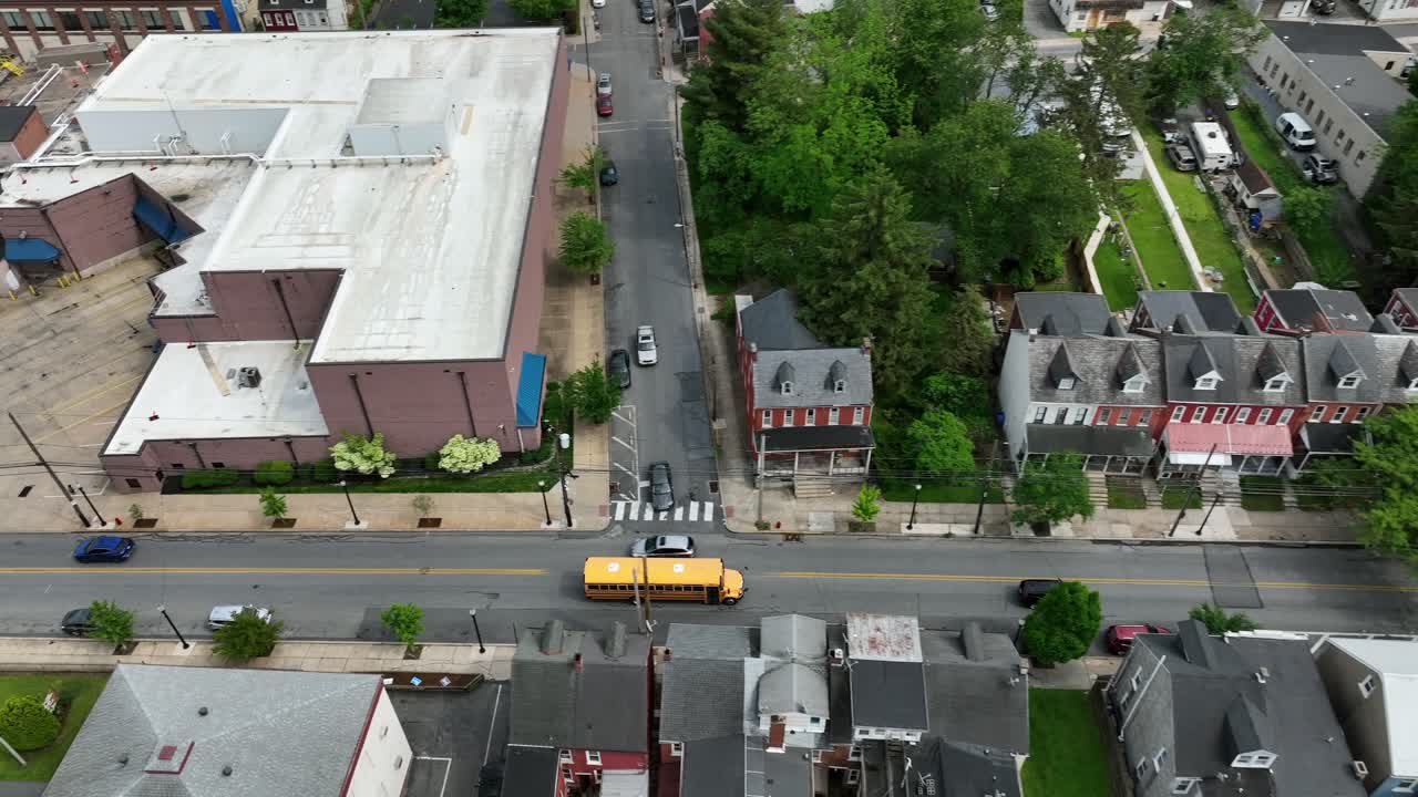 Aerial tilt up of yellow school bus on street of american town during cloudy day. Transport for pupils and children after school in spring. Traffic scene in american city. Historic town of Lancaster.