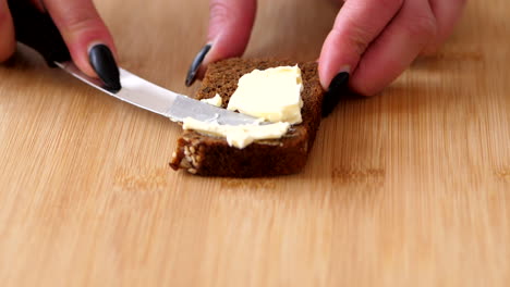 spreading a creamy butter on the slice of bread in the wooden chopping board