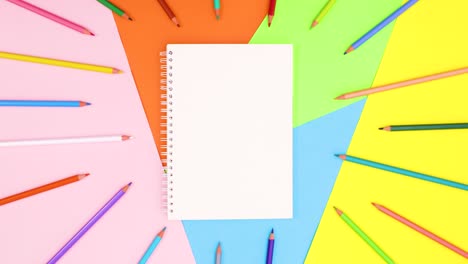 los lápices de colores se mueven alrededor del cuaderno abierto en un tema colorido. detenga el movimiento