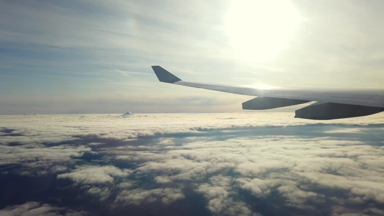 Passengers can enjoy a stunning sunset above the clouds as the airplane flies high in the sky. The wing frames the beautiful, glowing horizon and the fluffy clouds below
