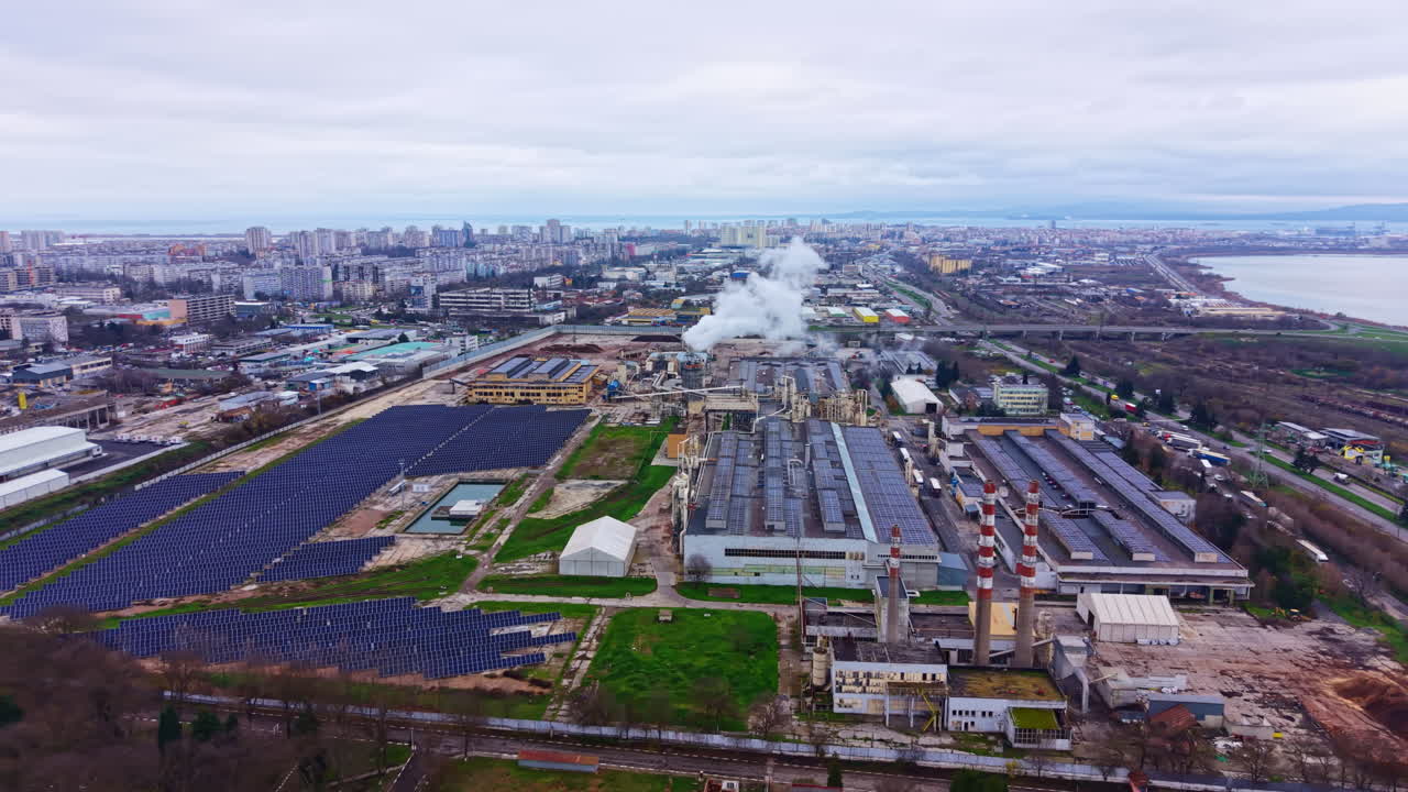 View of an industrial area with factories, solar panels, and a city skyline during cloudy weather