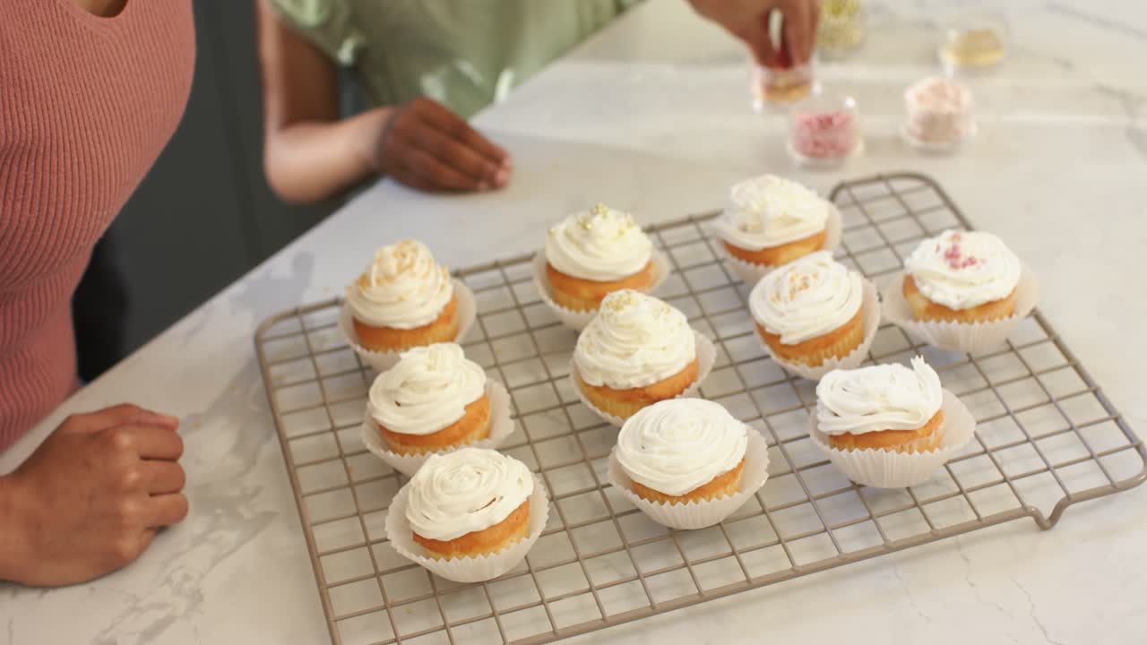 Mãe e filha diversas colocando granulados e decorando cupcakes cobertos com glacê no balcão da cozinha