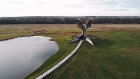 giant stone flower memrial site for victims of ustasa during world war 2 next to a small lake on a green meadow on a calm day