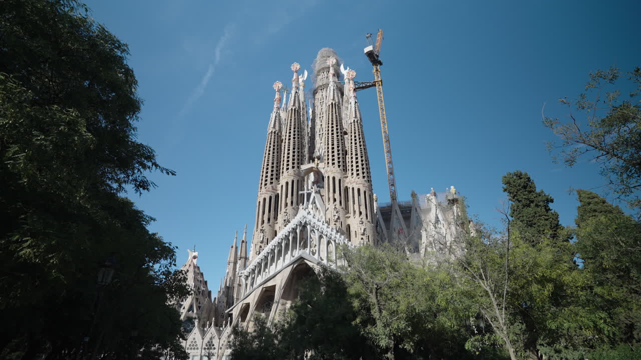 L'iconica Basilica della Sagrada Familia si erge sopra alberi verdi e lussureggianti sotto un cielo azzurro e limpido a Barcellona, Spagna