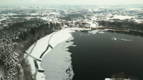 Frozen-lake-surrounded-by-a-snowy-forest-from-a-bird's-eye-view