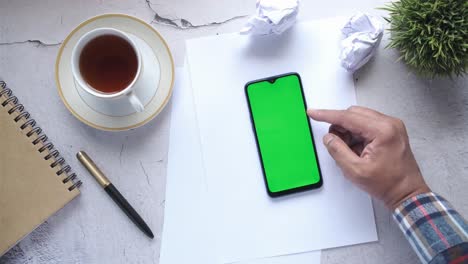 persona que utiliza un teléfono inteligente con pantalla verde en un escritorio