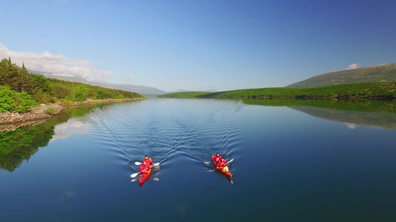 Giornata di sole tranquilla su un lago. Drone che vola in avanti sopra 2 kayak. Uccelli che volano sul lato sinistro