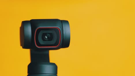 mechanical gimbal camera lens rotates on yellow background, robotic camera macro