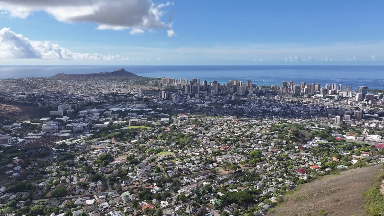 Aerial drone footage overlooking the Honolulu skyline on Oahu, Hawaii, showcasing high-rise hotels, tropical coastline, blue ocean waters, and the scenic cityscape of Waikiki under sunny skies