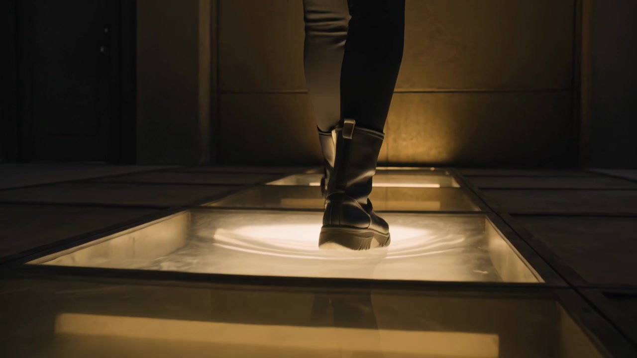 Stepping black boot on lit panels starting woman walking down hall toward warm glow, panels glint