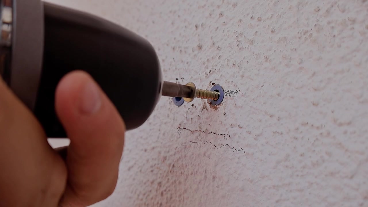 Hand drives screw into textured wall. Tool grips screw firmly for secure fastening. Close-up shows focused, deliberate motion. Ideal for DIY, home repair, or construction projects