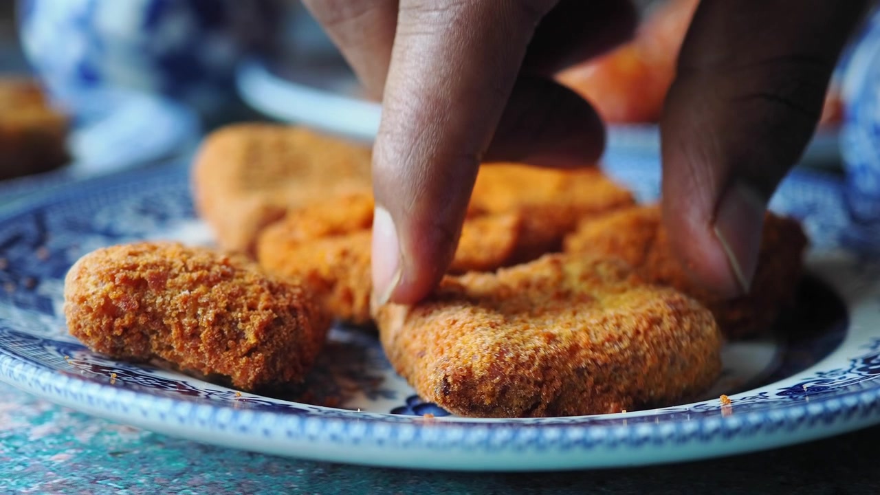 Mano cogiendo un nugget de pollo frito crujiente de un plato decorativo