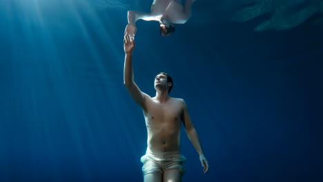 man underwater reaching towards the surface with his reflection visible above