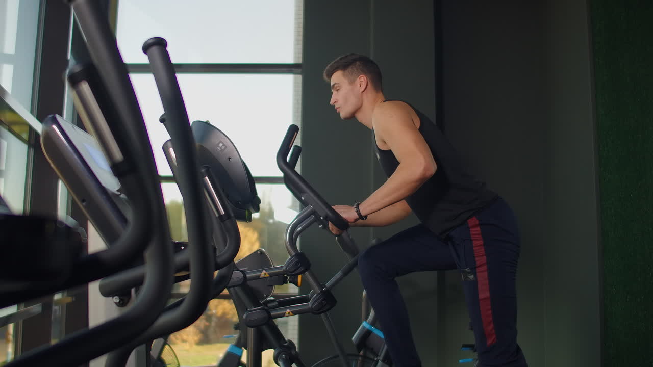 Beautiful fit sportive positive young man in gym doing exercises on elliptical trainer working out.