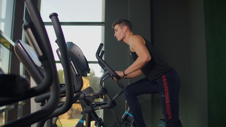 Beautiful fit sportive positive young man in gym doing exercises on elliptical trainer working out.