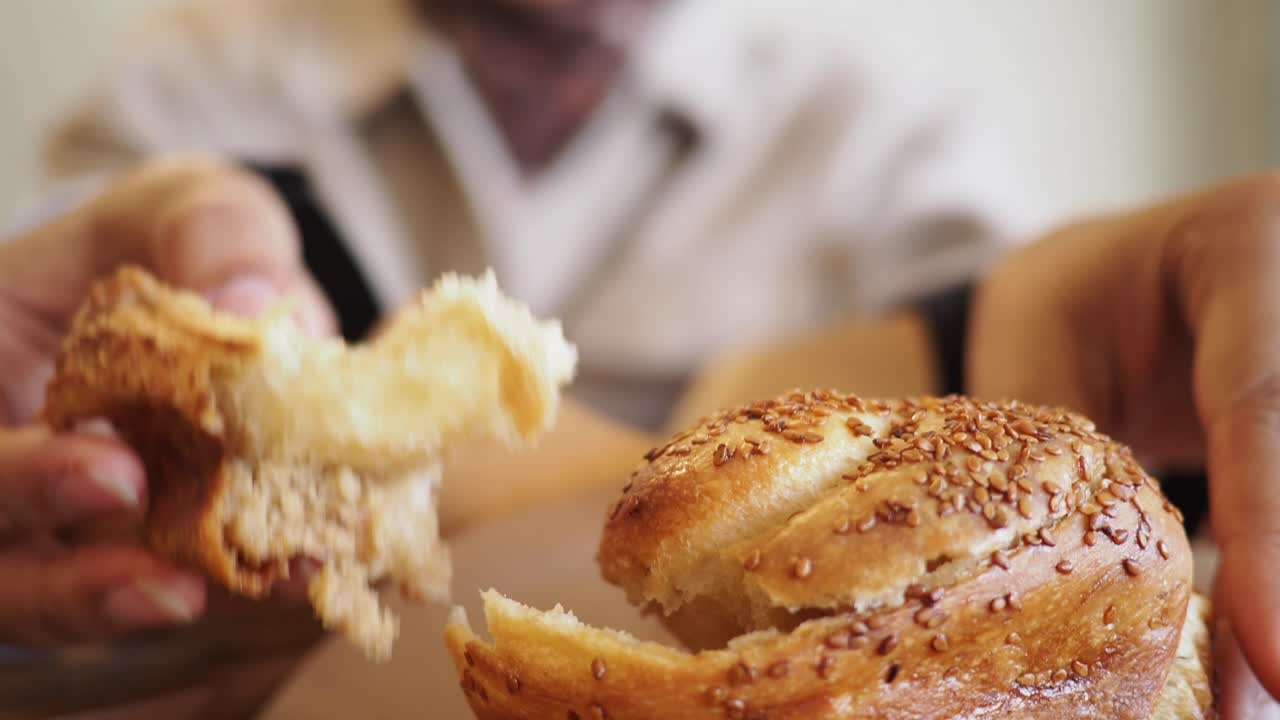 Close-up of Hands Tearing a Fresh Sesame Seed Bun