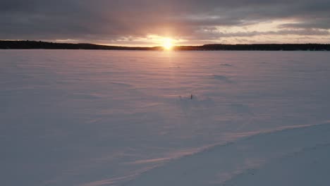 wind blows across the snow and over two ice fishing traps at sunset aerial