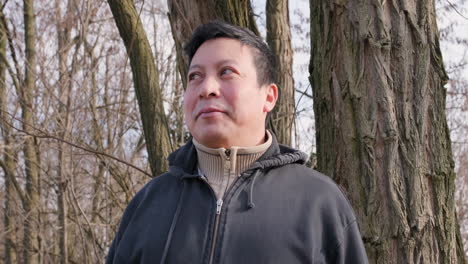 portrait of a man in sweatshirt looking around in the forest with the sun on his face during a winter afternoon - slow motion shot