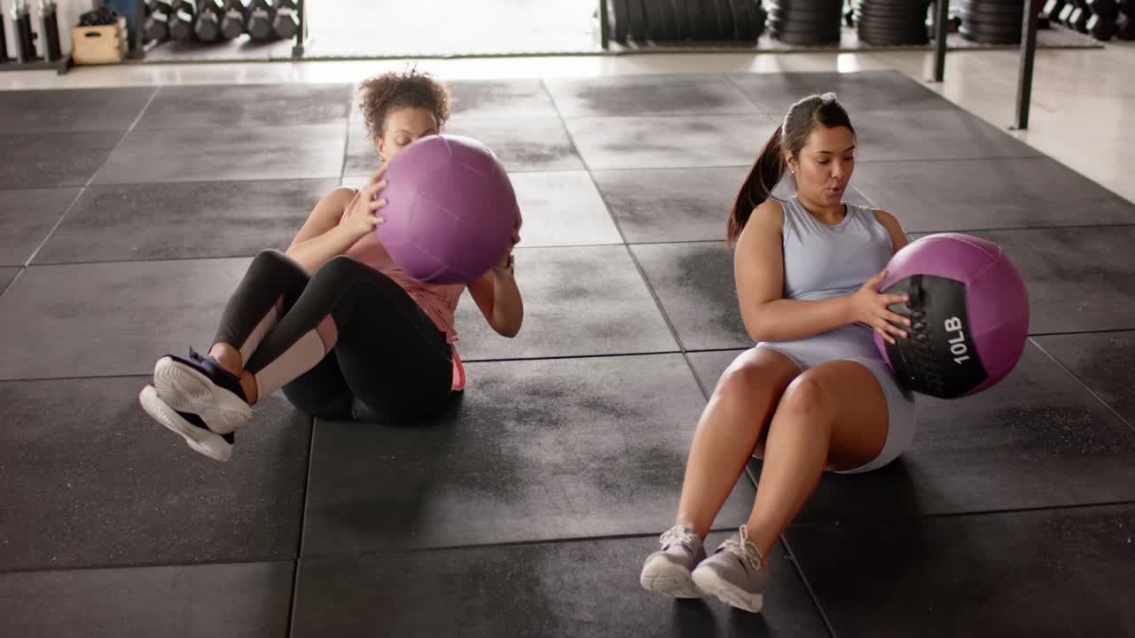 For core workout Diverse female friends in sportswear twisting with purple medicine balls in gym