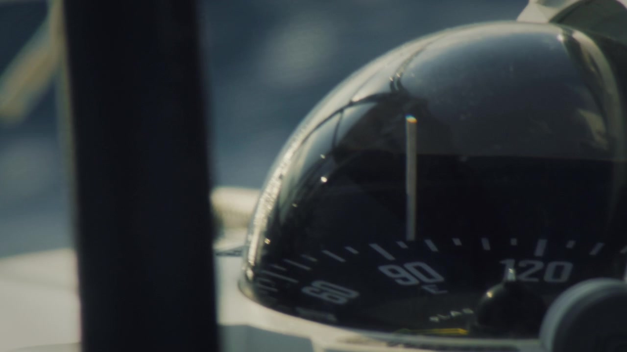 Marine compass close up with dynamic water rushing past in the background - cinematic focus pull shot of boat compass on fast moving yacht filmed on vintage lens.