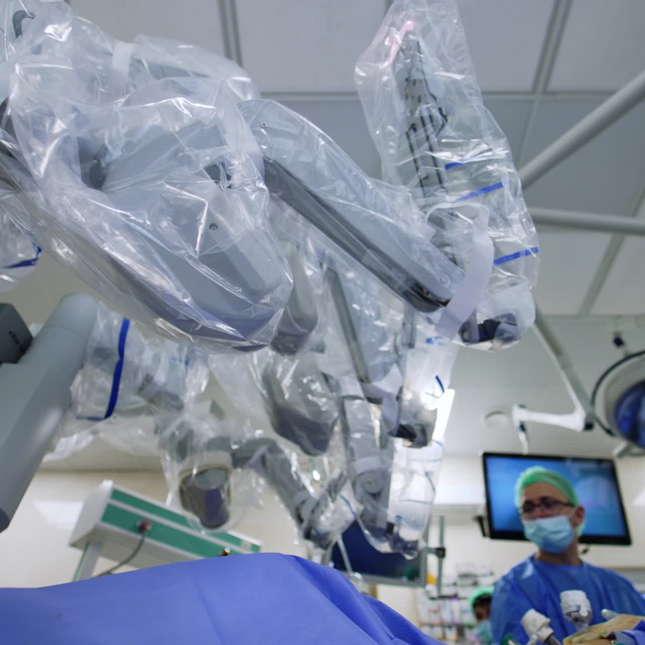 Closer look on the multiple robotic arms of a surgeon robot. Innovative medical equipment covered in plastic. Low angle view