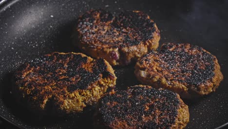 rociar aceite sobre buñuelos de atún frito marrón en una sartén negra y cerrar la sartén con tapa