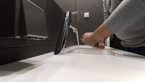 the man washes his hands by the sink, a modern bathroom in grey colours and a white sink, static video