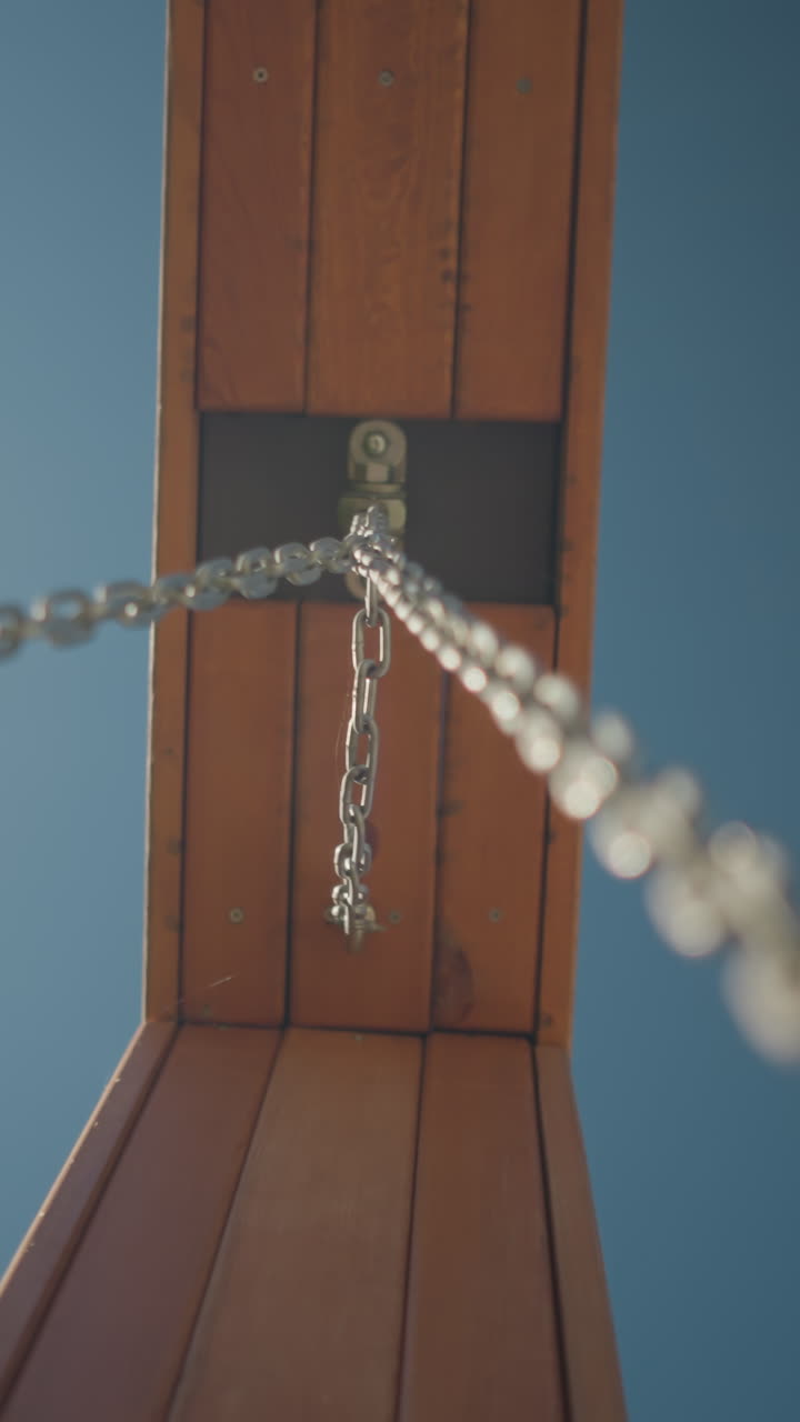 나무 프레임에 부착된 금속 사슬의 클로즈업, 밝은 파란 하늘을 배경으로 낮은 각도에서 포착, 산업의 힘과 자연 재료가 야외 풍경과 여있는 것을 보여줍니다.