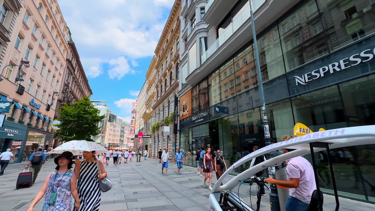 Vienna, Austria - June 9, 2025: Lots of people walk by the pedestrian street with modern shops. Walk by the old town of Vienna, Austria