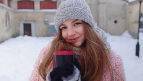 stylish woman traveler with hot drink in cup looking around through city street during vacations