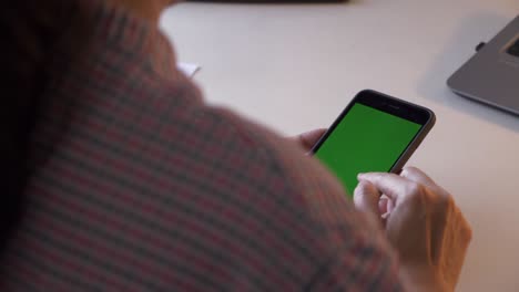 sobre el hombro, empujón, primer plano de una persona irreconocible usando un teléfono inteligente, deslizando la pantalla verde.