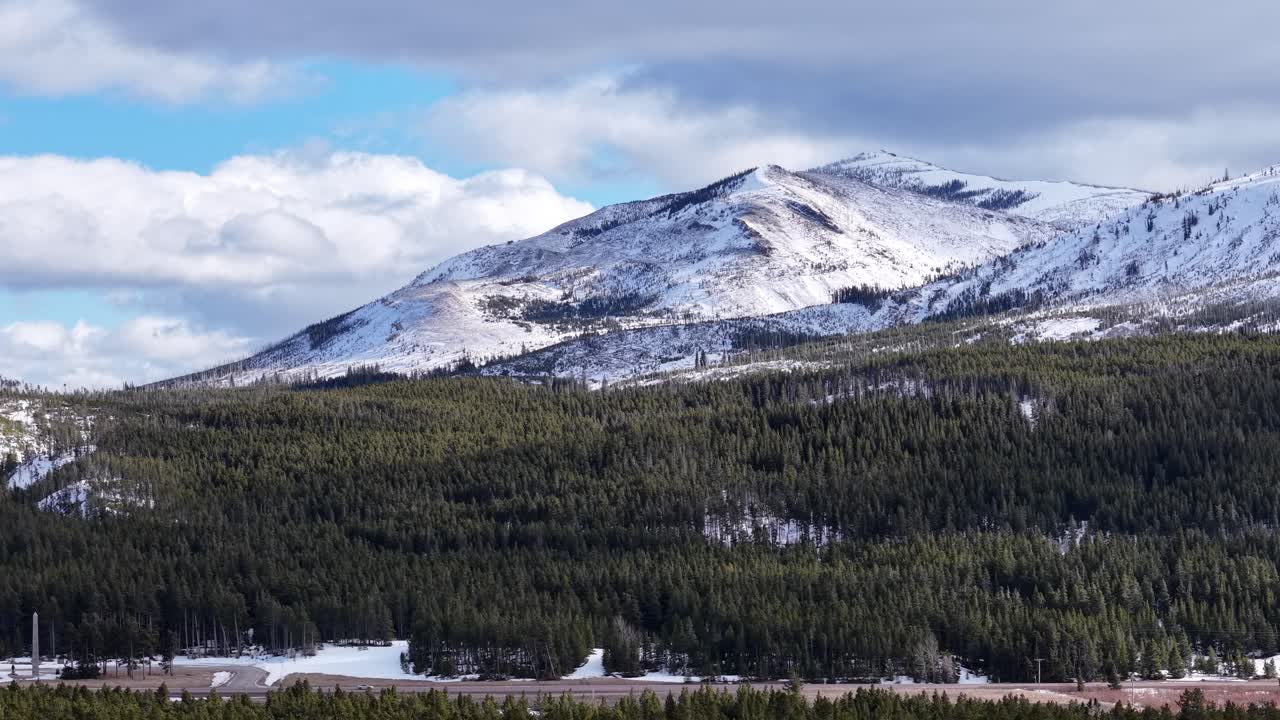 Ripresa con drone di una catena montuosa innevata sopra una fitta foresta e un fiume che si snoda nel Parco Nazionale Glacier, Montana.