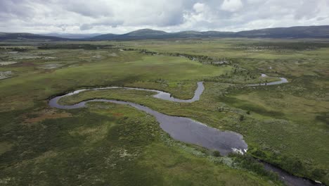 Small-tundra-river-meanders-through-flat-Norway-landscape,-aerial