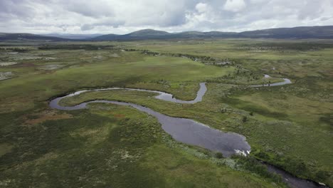 small tundra river meanders through flat norway landscape, aerial