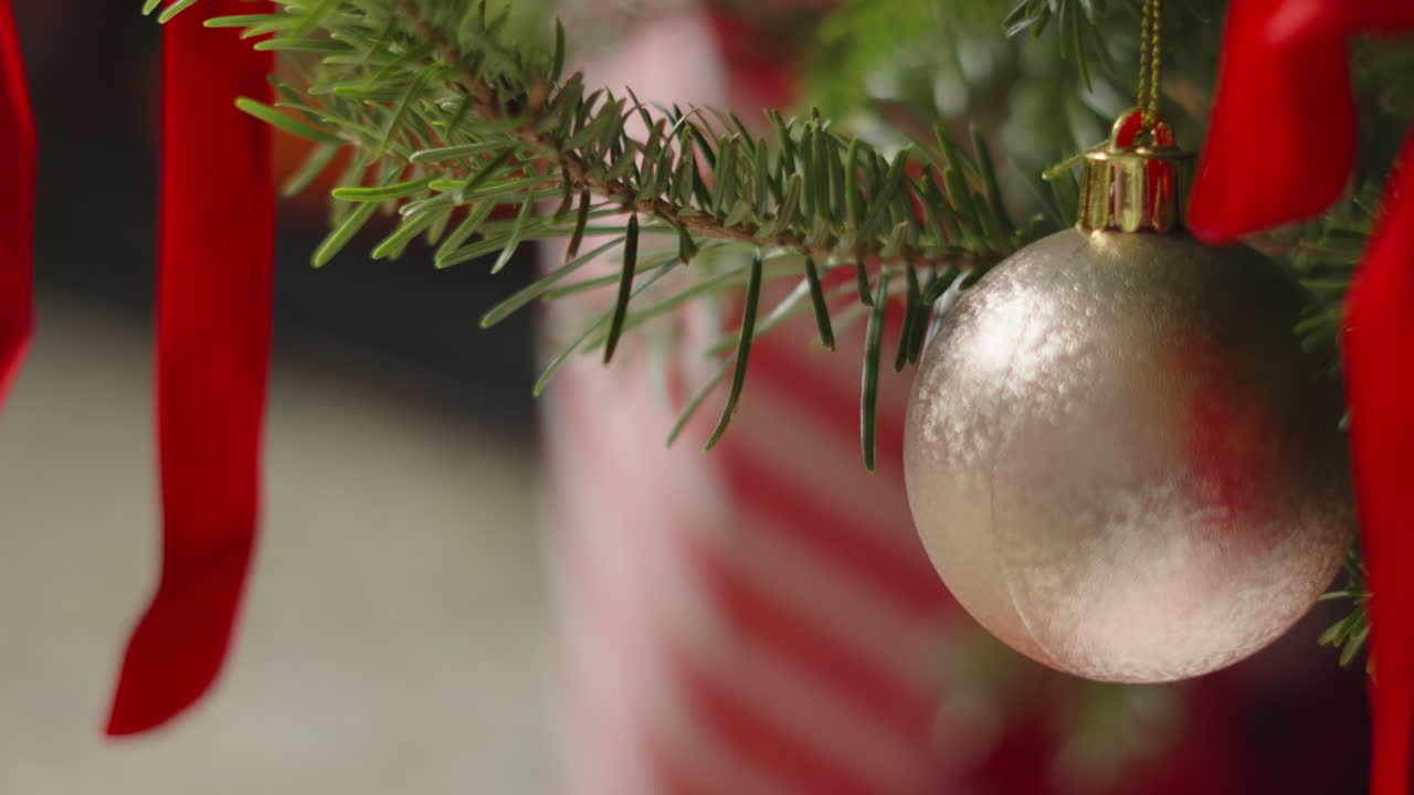 Silver Christmas Bauble Hanging on Xmas Tree with Bows and Presents By Santa Below in Cozy Home Environment. Happy Merry Festive Seasonal Decoration