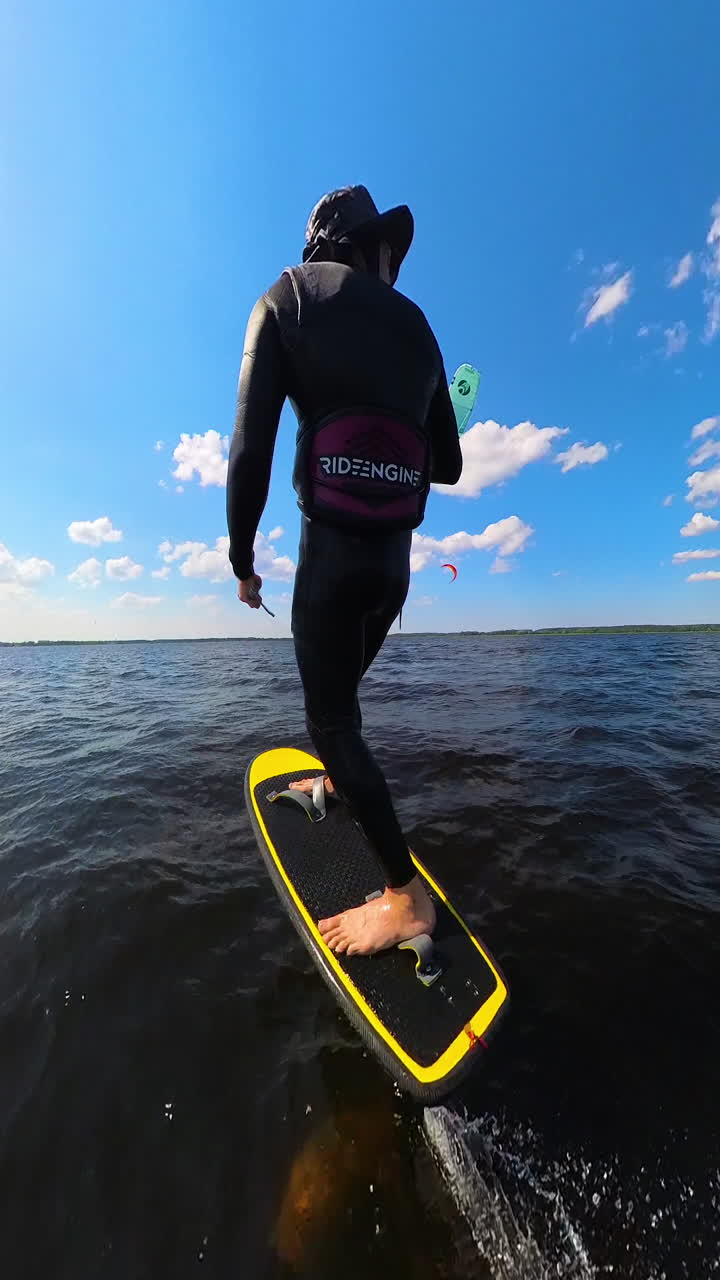 Vertical - Kiteboarder In Wetsuit Riding On Hydrofoil Board, Being Towed By Teal Kite In Distance. rear shot