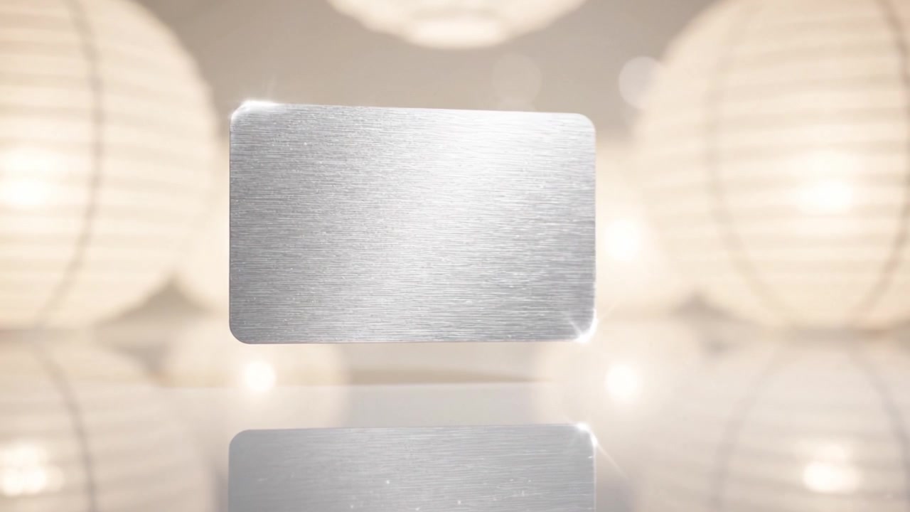 Una carta metallica elegante e riflettente, esposta in modo prominente su uno sfondo delicatamente illuminato, circondata da eleganti lanterne, che mette in mostra design moderno e minimalismo.