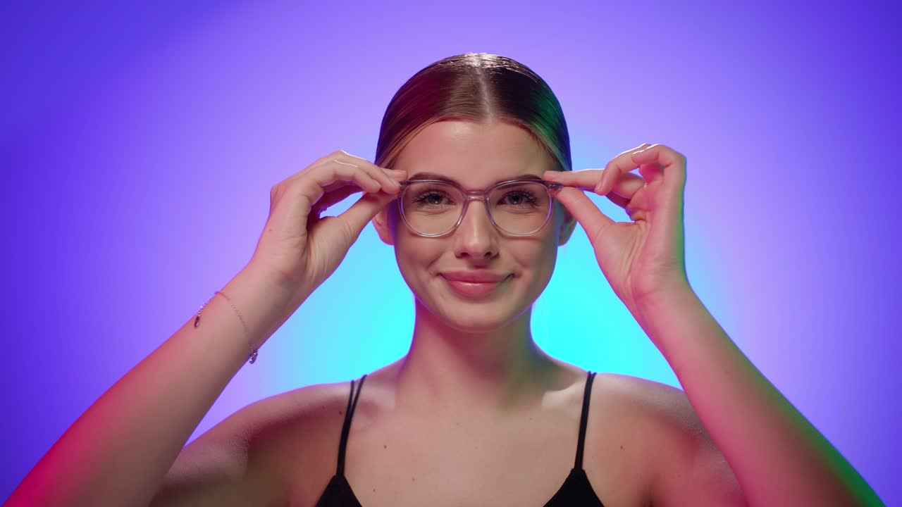 joven mujer rubia caucásica se pone sus gafas de vidrio observando y sonriendo a la cámara felizmente, cerca de la toma de estudio