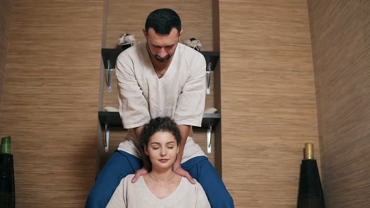 atractiva masajista tailandesa está masajeando la cabeza de una mujer joven sentada detrás de ella 1