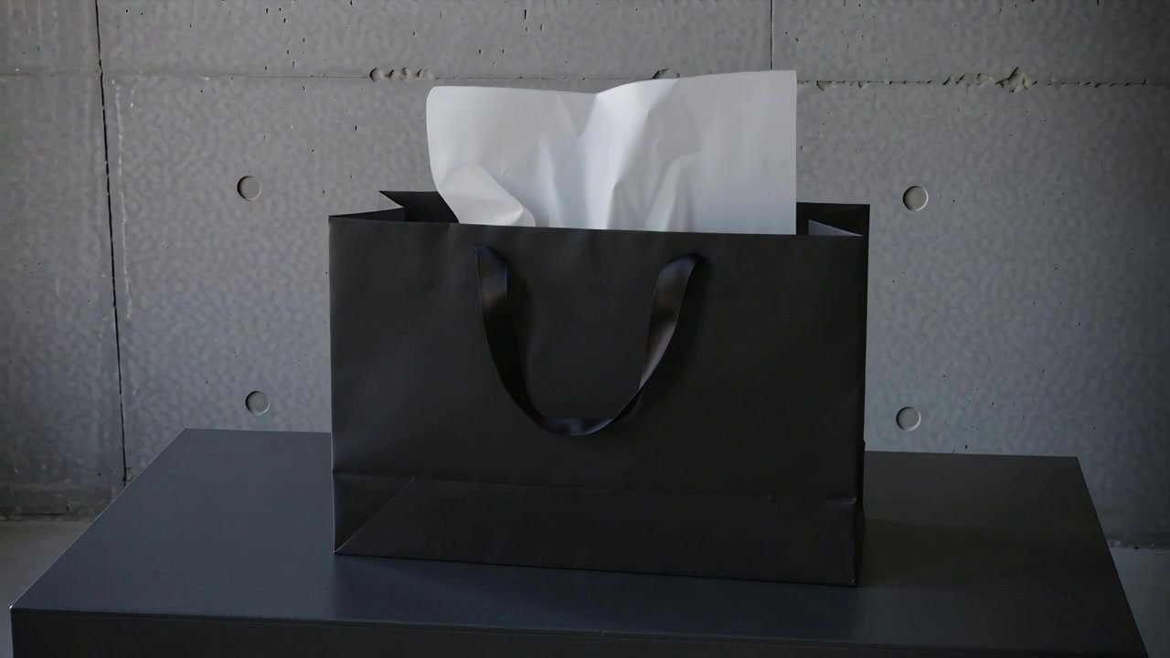 Ripresa dall'interno che solleva un fazzoletto bianco da una borsa nera opaca su un piedistallo da studio, rivelandone il contenuto