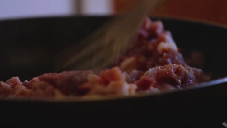 man is stirring bacon with a fork in a frying pan