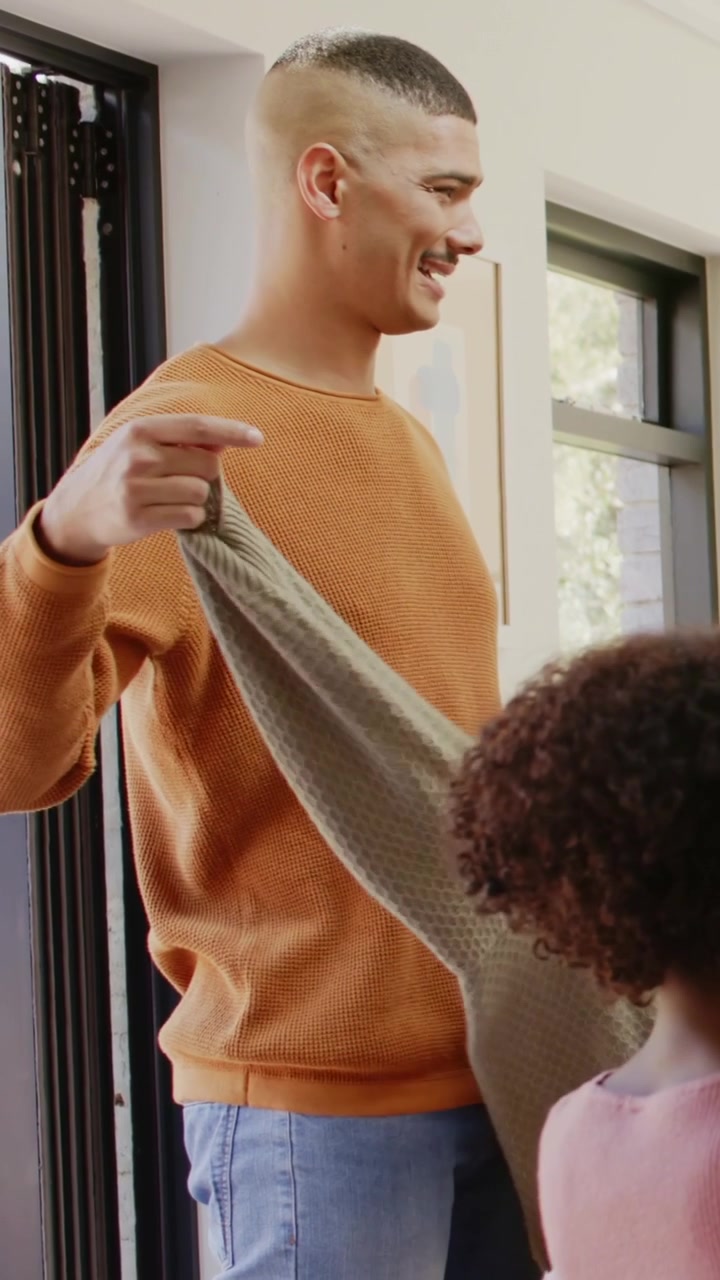 Vertical video: Picking green knit sweater from pile dad in rust sweater unfolding at table for kid