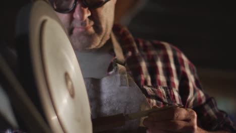 primer plano de un hombre caucásico fabricante de cuchillos en un taller con gafas y usando una lijadora