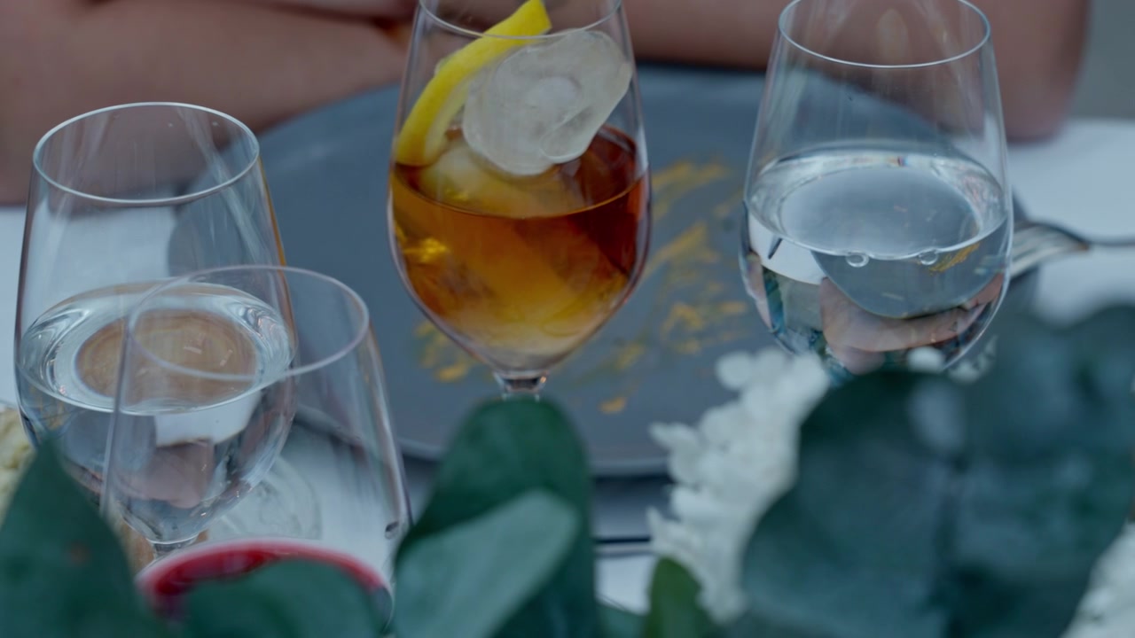 Vasos de agua, un cóctel con limón y una copa de vino tinto en una mesa puesta, indicando un evento de catering.
