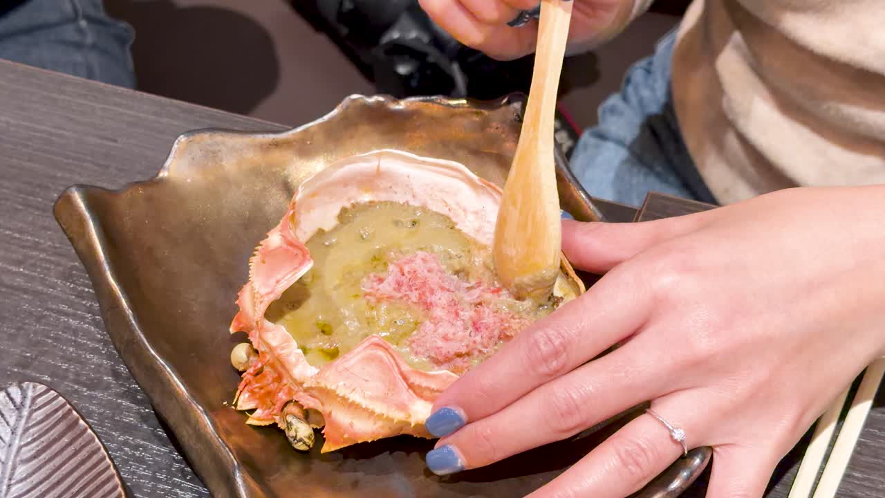Primo piano di mani che usano un cucchiaio di legno per mescolare carne di granchio all'interno di un guscio